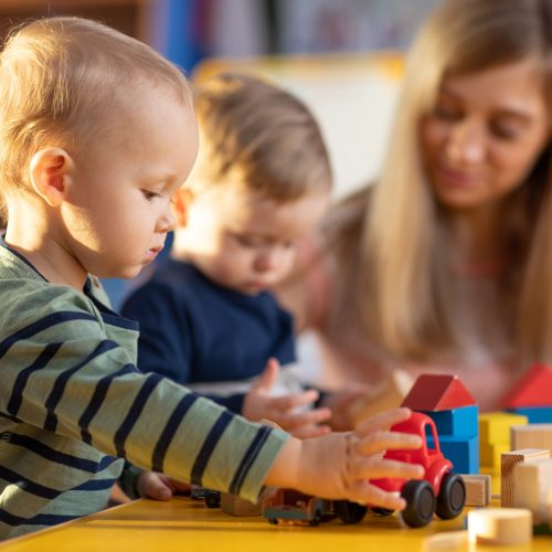 Preschool teacher and cute kids boys playing in kindergarten